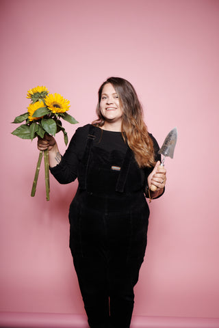 Tatyana, Co-Founder of The Mini Gardeners Club holding sunflowers and a trowel