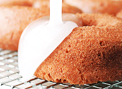 Animated GIF of a plain doughnut being coated with a white cream glaze, with the glaze dripping down the sides of the doughnut.