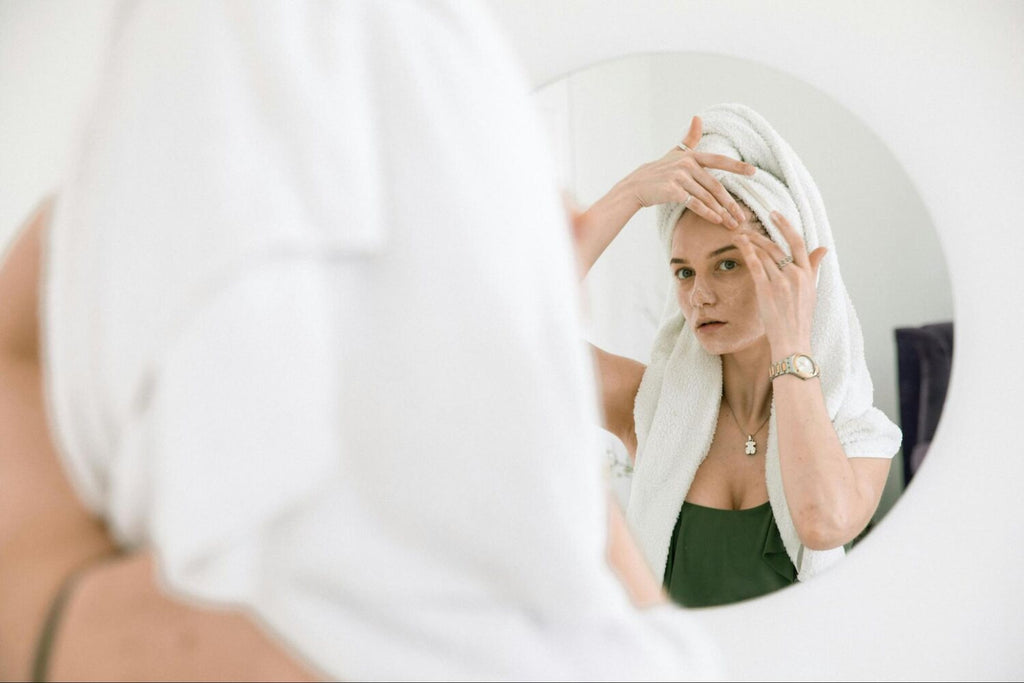 a woman applying cream to her face in front of a mirror