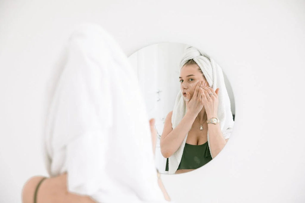 A woman looking in the mirror while exfoliating her skin