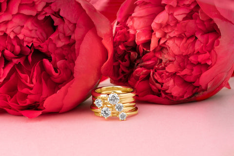 4 goldene Verlobungsringe mit Diamanten die aufeinander gelegt sind und im Hintergrund sind 2 Rosen