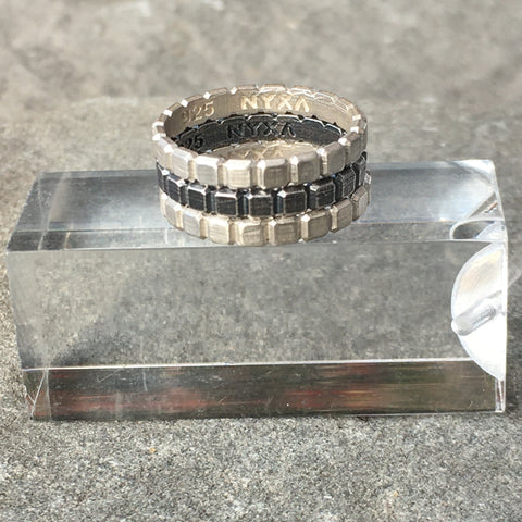 Three Faceted Cushion Cut Sterling Silver Stacker Rings stacked on top of each other and sitting on top of a clear acrylic block. A blackened patina has been applied to the middle ring.