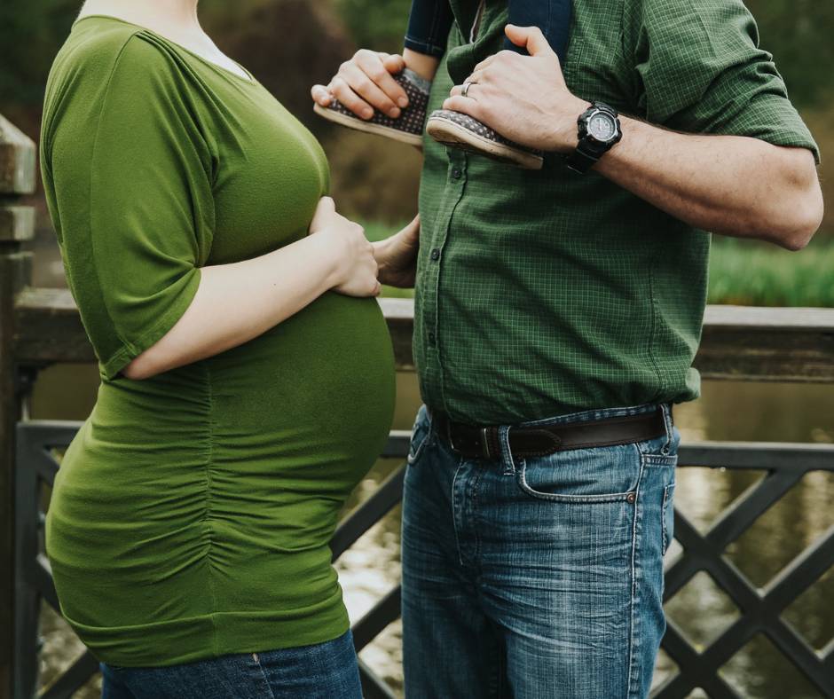 Couple facing each other while mom puts hand on her pregnant belly