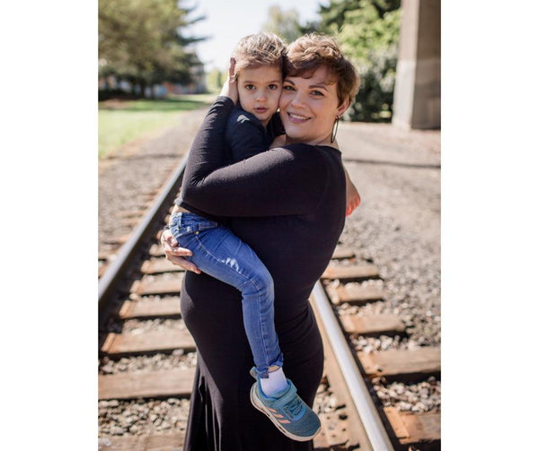 Pregnant mother holding her daughter while standing on train tracks at Cathedral Park in Portland, OR