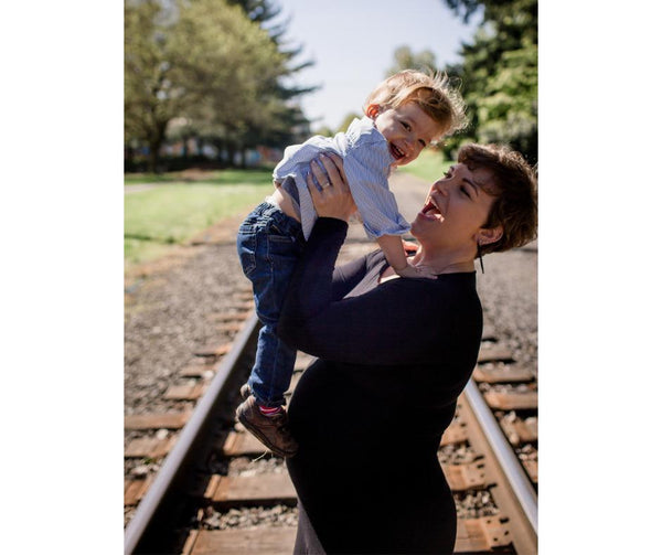 Pregnant mother tossing her son in the air while standing on train tracks at Cathedral Park in Portland, OR