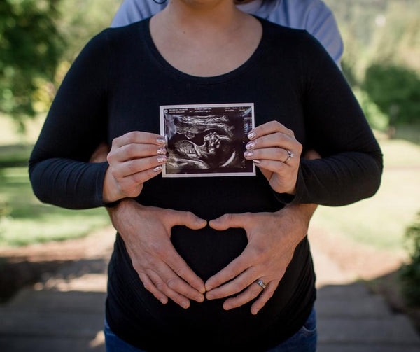 Pregnant woman holding ultrasound photo while her husband has his hands in a heart shape over her belly
