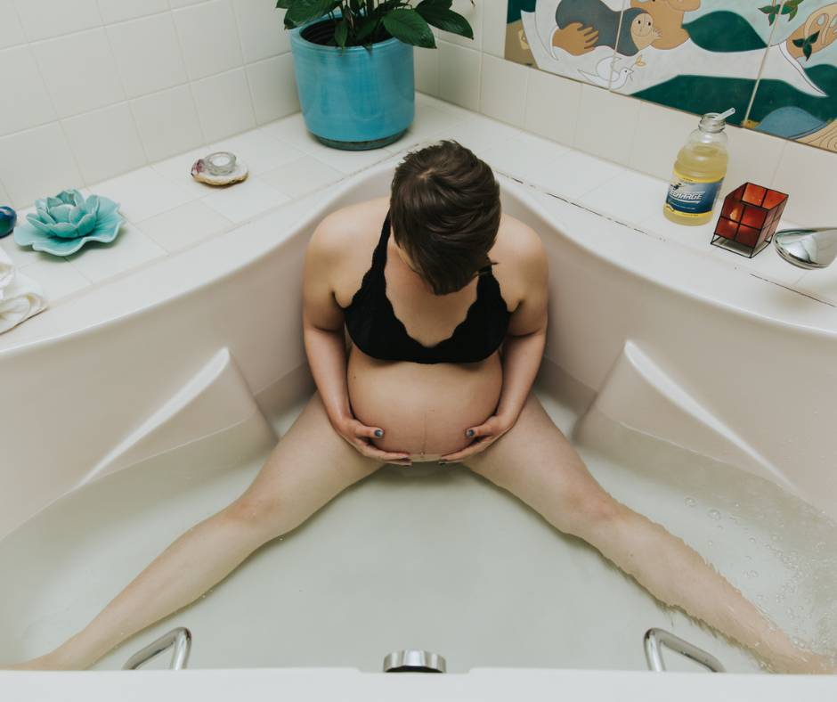 Pregnant woman in a large bathtub looking down and holding her belly