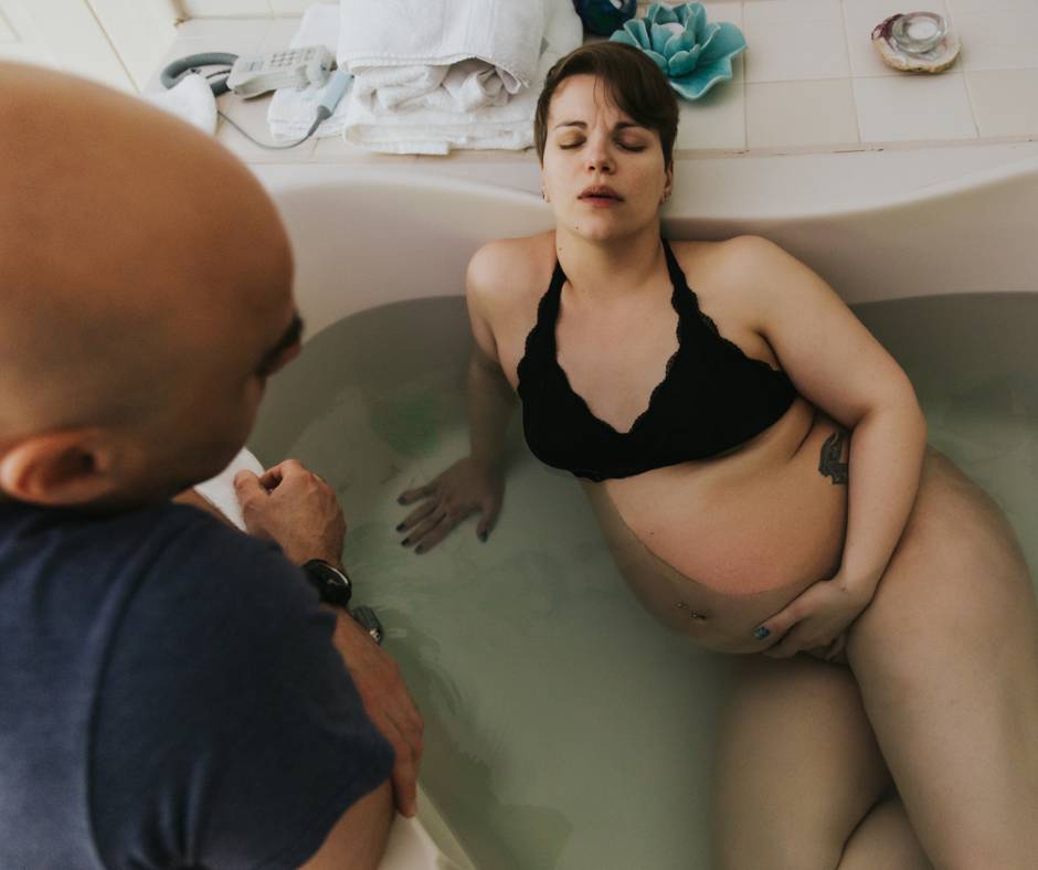 Pregnant woman laboring in a large bathtub with her husband kindly looking at her