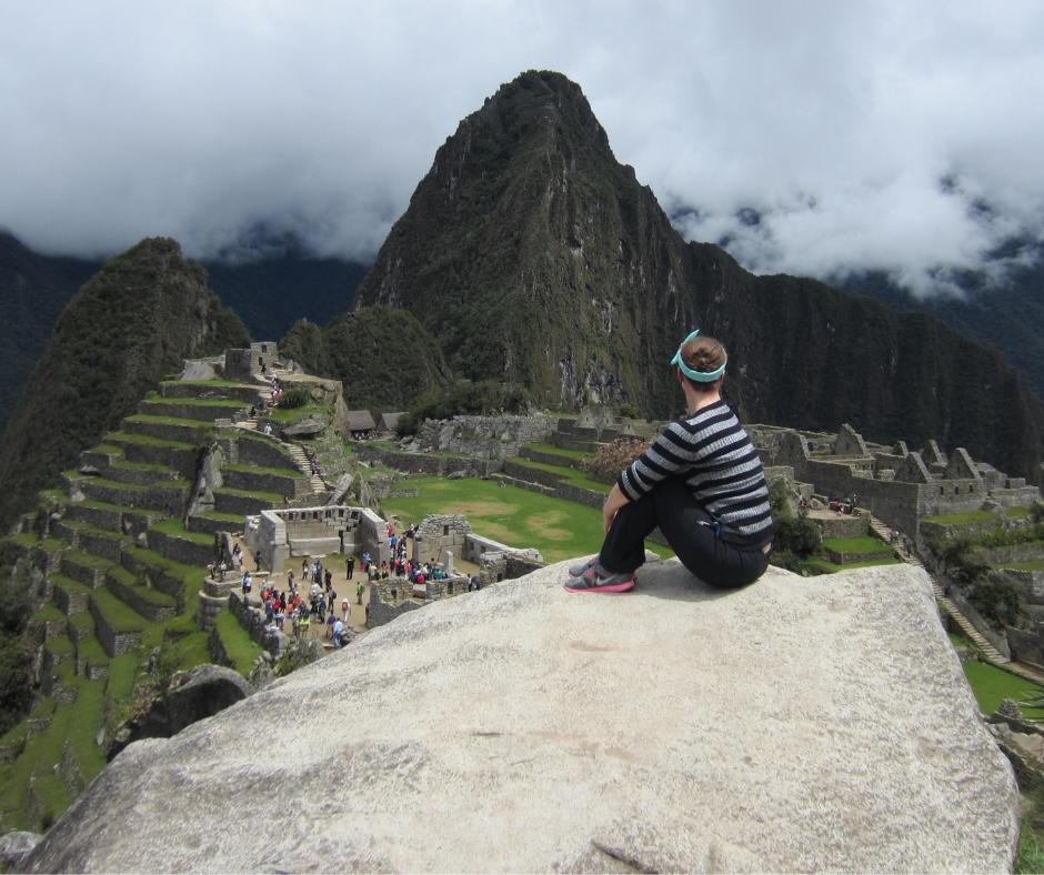 Woman sitting on top of large rock overlooking Machu Picchu in Peru