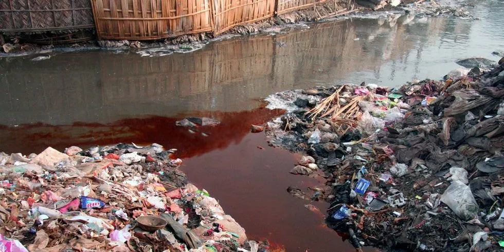 River in China surrounded by plastic and trash that is contaminated with red dye from clothing manufacturing