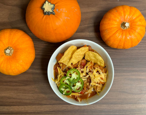 Pumpkin chili topped with chips, jalapeños and cheese, surrounded by pumpkins