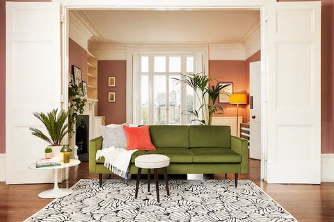 Green velvet sofa with throw and cushions in front of orange wall