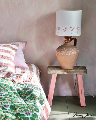 Bed with Pink Painted Table and Stencilled Lamp with pink textured wall