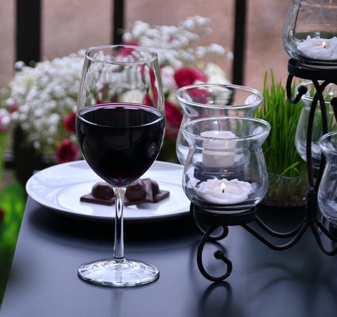 A glass of red wine in front of a plate of chocolate, next to dimly lit tea lights.