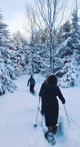 Two people snowshoeing through snowy ground and snow-covered trees.