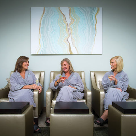 Three women in robes sitting in spa chairs enjoying a beverage.