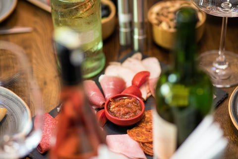 A charcuterie board with tomatoes, sauce, and various sliced meats surrounded by Rove wines.
