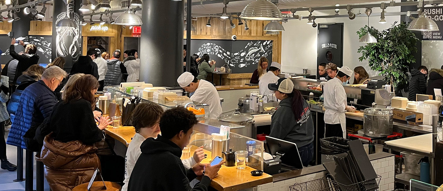 View of a fish market with people eating at its sushi bar.