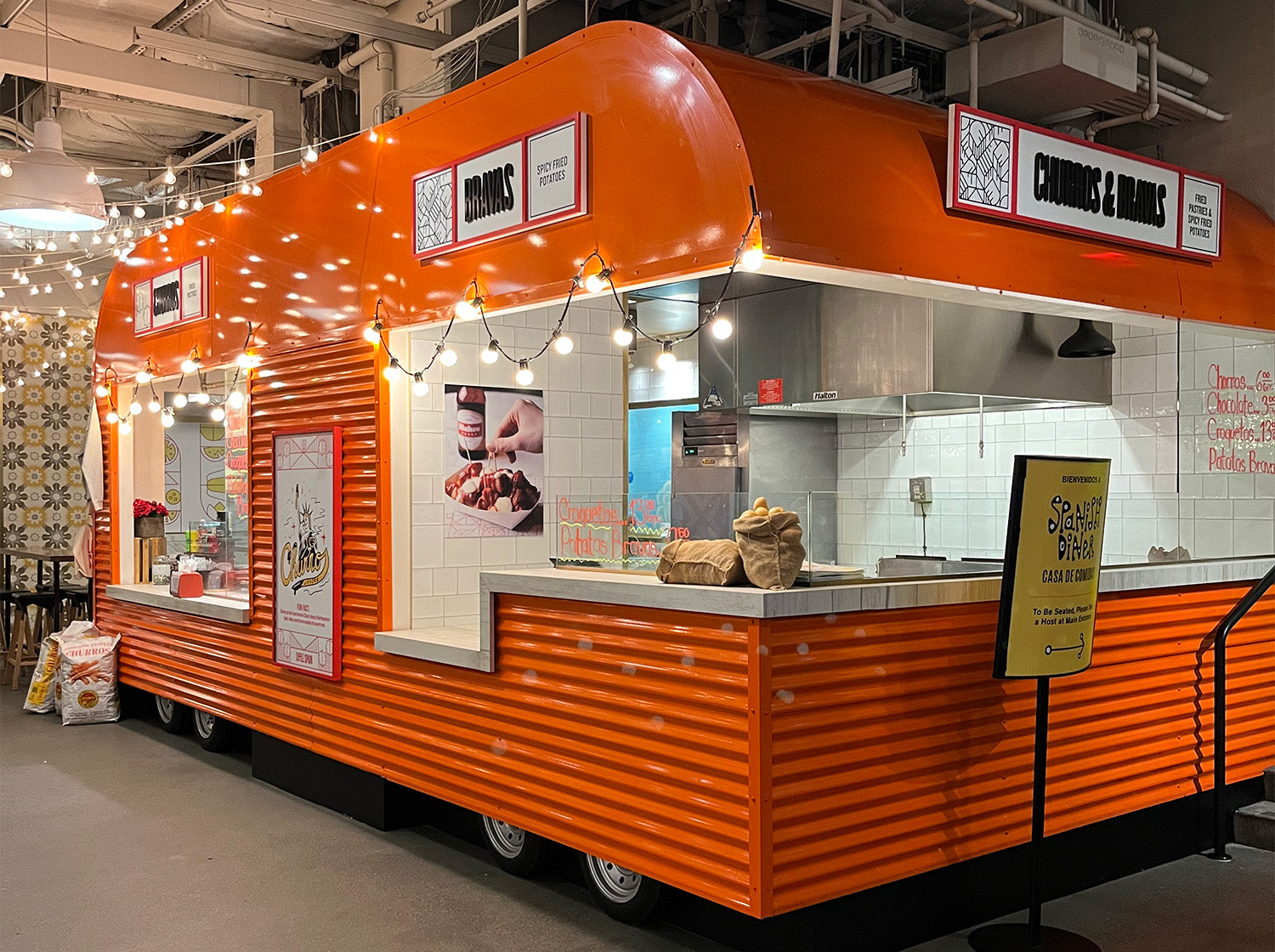 Shiney orange colored food truck that serves Spanish cuisine.