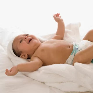 Baby lies on the bed and stretches his arms in the air while crying