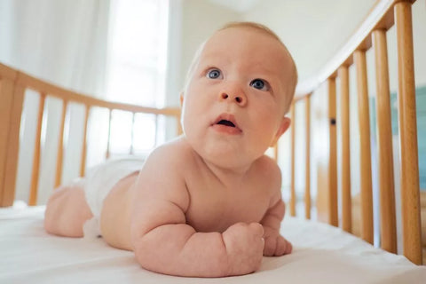 Baby krabbelt im Babybett und schaut in die Kamera