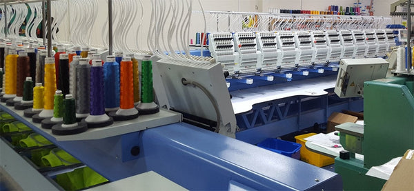 A row of Embroidery machines, in the foreground multicoloured thread on the rear of the machines. 