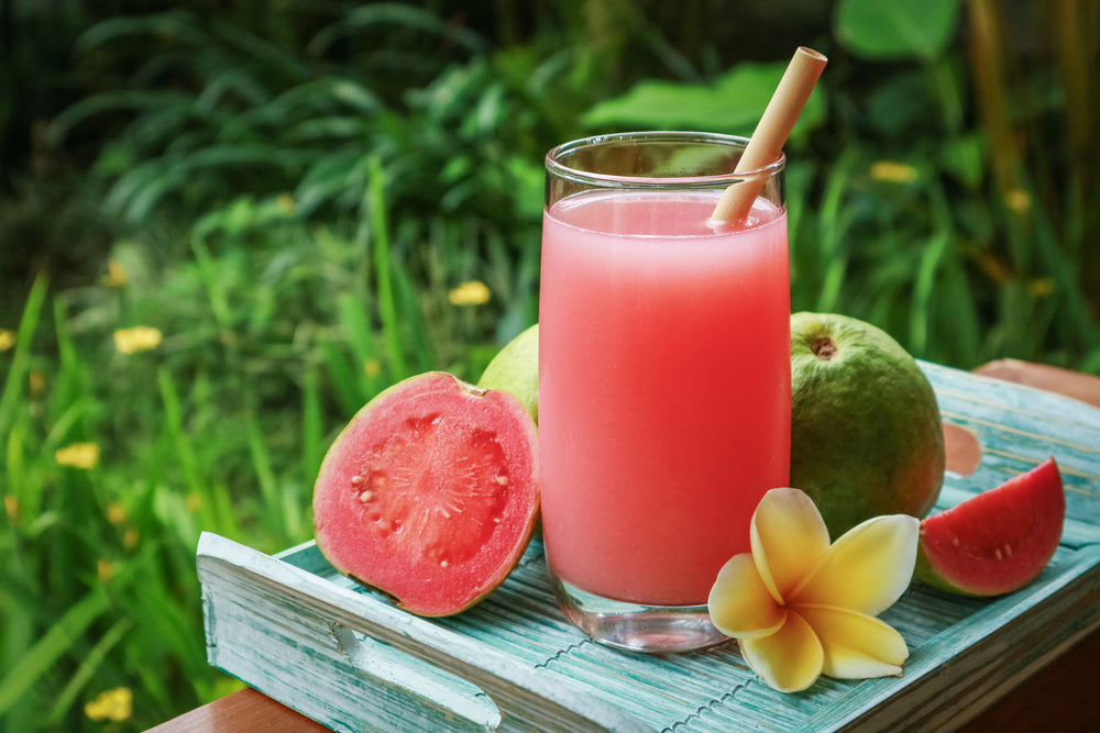 glass with a cold red beverage with a brown straw with guava and flowers