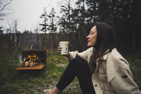 Taper sur la route assis devant un feu de camp à Terre-Neuve avec une bière fraîche dans une tasse isotherme en acier inoxydable à emporter à la main