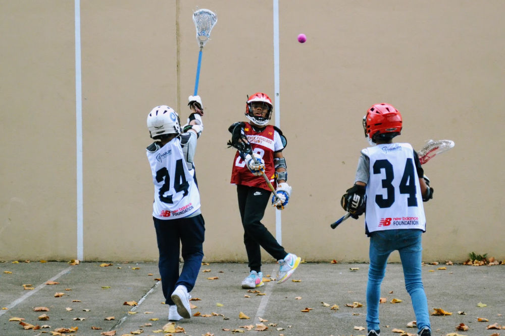 Girls from Harlem Lacrosse playing on hard concrete surface