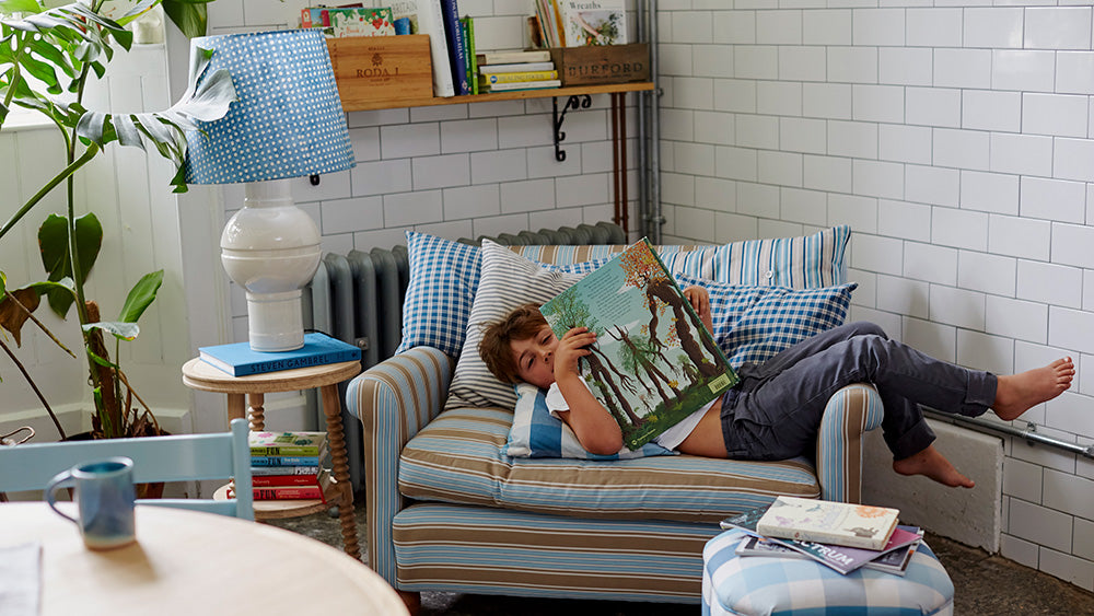 A young boy reading a book on a NiX love seat in a living room.