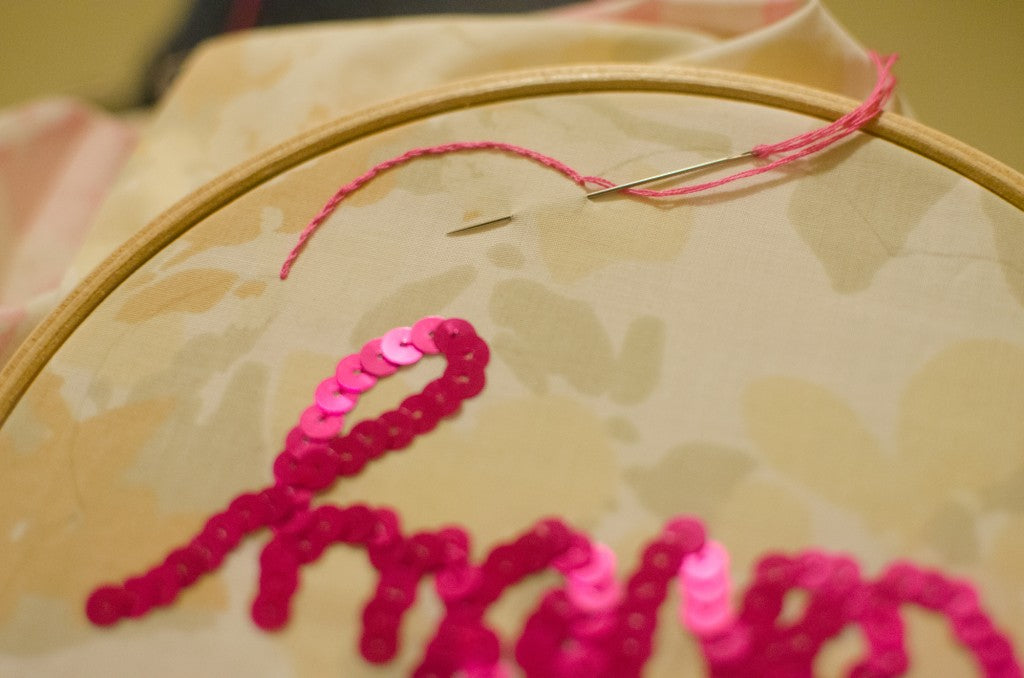 Pink embroidery being sewn on to a vintage floral fabric in an embroidery hoop