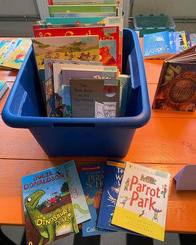 A blue tub of books with a few more scattered on the orange table.