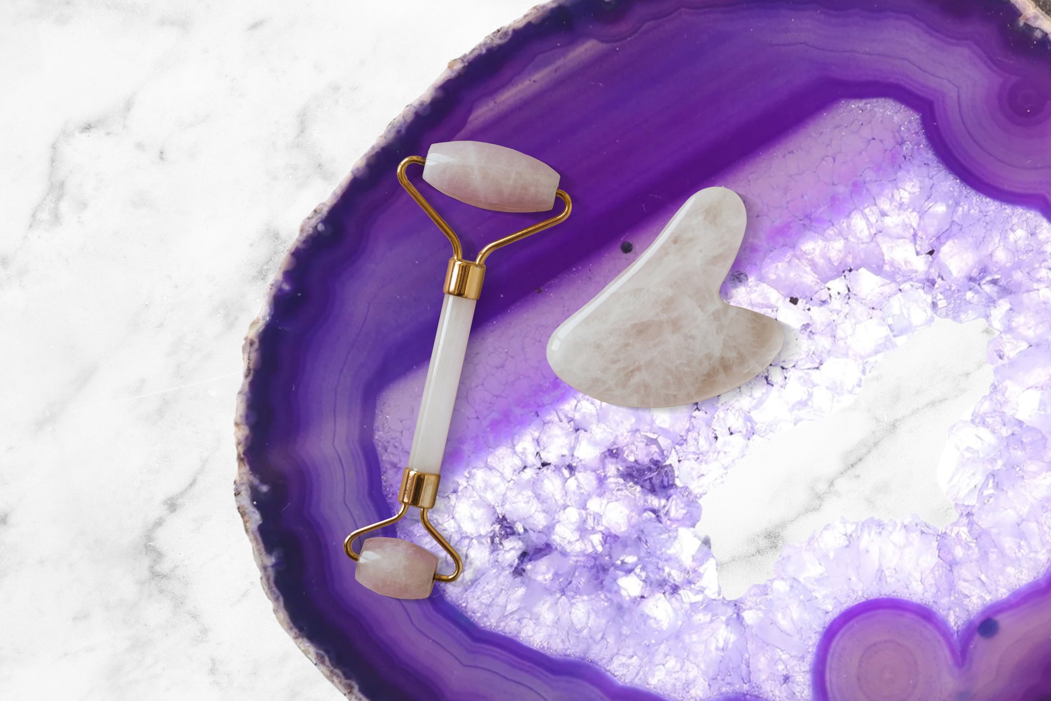 A rose quartz skin roller and gua sha set on a purple agate slice