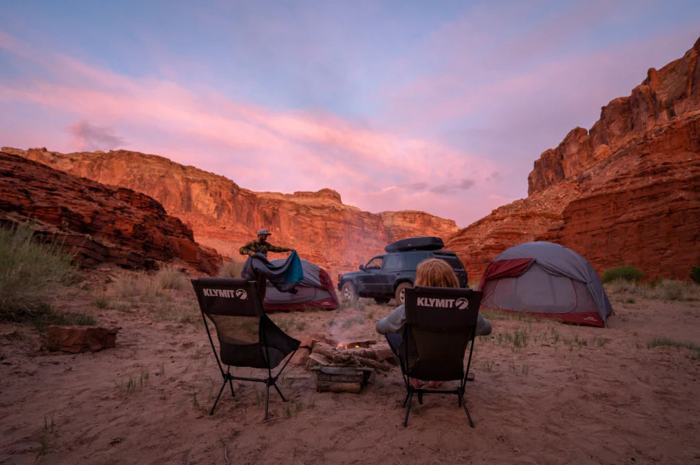 two people sitting in camping chairs at sunset