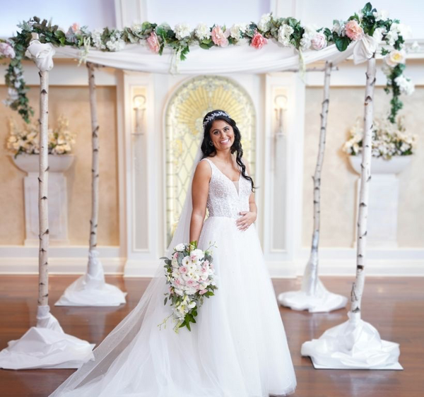 A bride holding a cascading bouquet of pink blooms and greenery under a flower-filled arch.