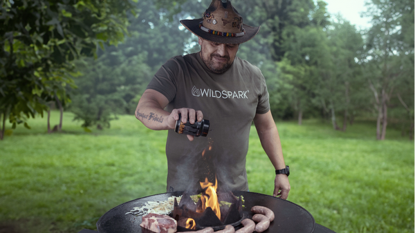Hawk Blackburn im Wildspark Classic Shirt aus Bio-Baumwolle grillt an der Feuerplatte Steaks, Gemüse und Bratwürste