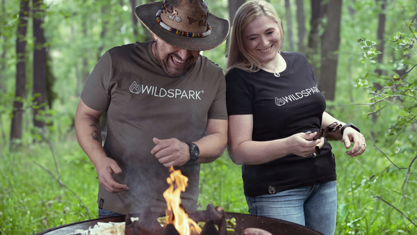 Maja und Hawk stehen zusammen am Grill und grillen zusammen. Beiden tragen das nachhaltige Wildspark Classic Shirt aus Bio-Baumwolle.