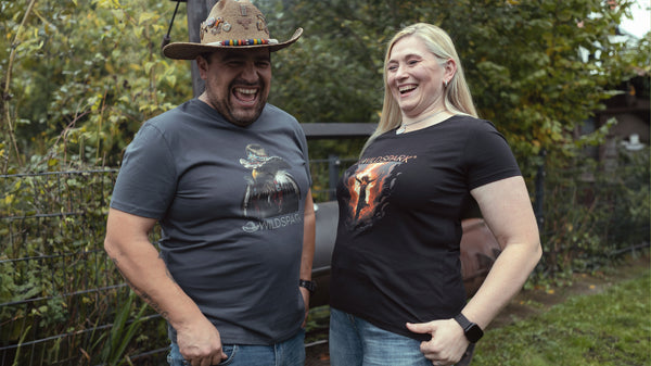 Maja und Hawk stehen vor einem amerikanischen BBQ Smoker. Beide tragen ihr eigenes Wildspark Signature Shirt aus Bio-Baumwolle.