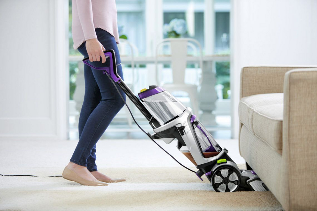 A woman using a Bissell ProHeat 2X Revolution Pet Upright Carpet Washer 2066F to clean under the couch