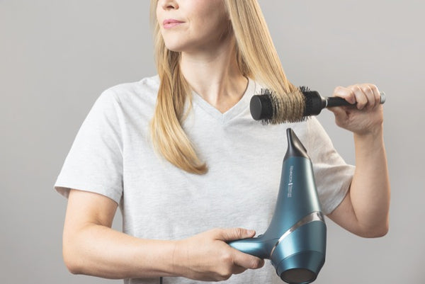 A woman with long blonde hair drying her hair with a Remington advanced coconut therapy dryer