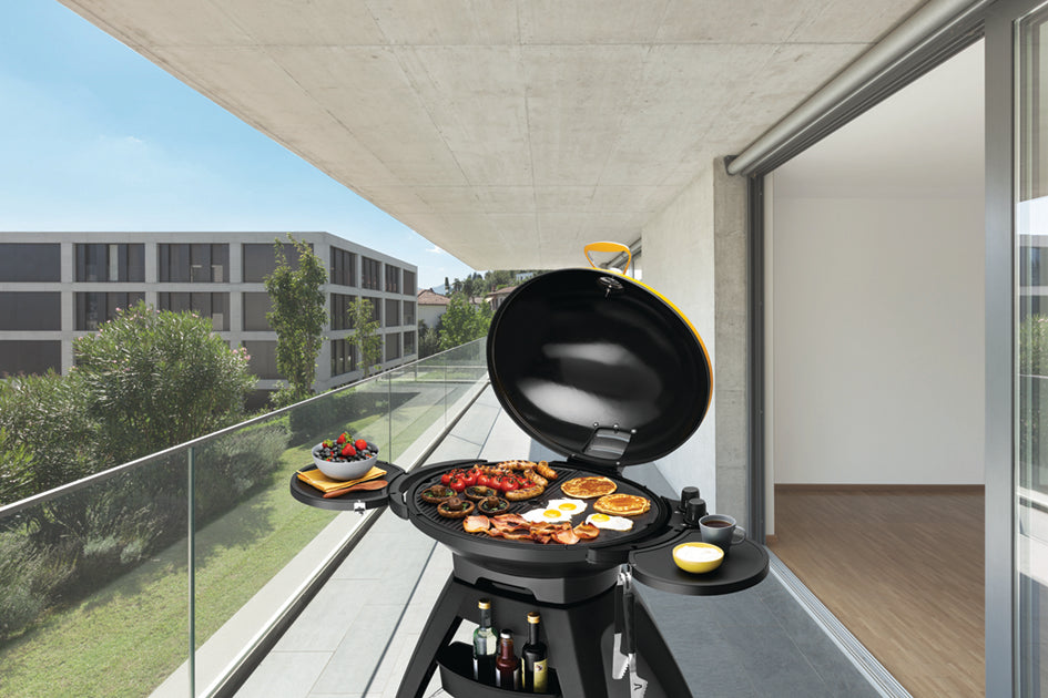 beefeater 10bugg portable bbq in amber colour on a balcony, cover open with food cooking