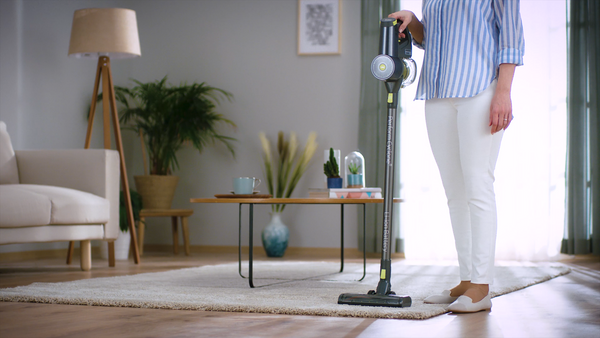 A woman in a blue and white striped shirt vacuuming a rug with a beko practiclean stickvac