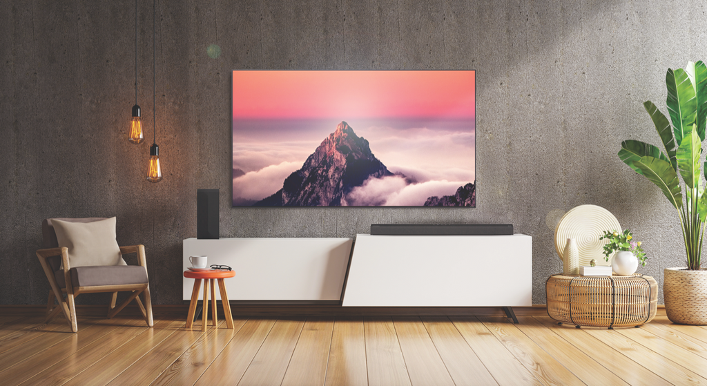 An LG QNED TV mounted on a dark brown wall with a sunset mountain view on the screen