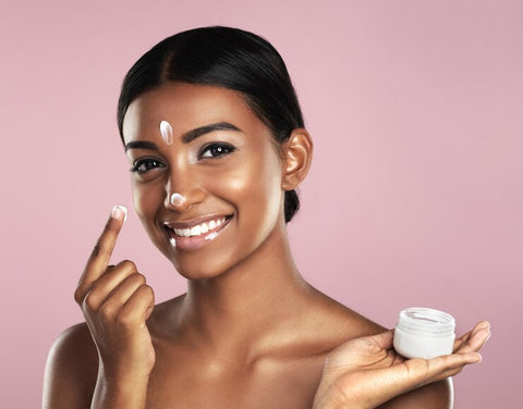 Black lady applying skincare product on her face to describe the use of azelaic acid and retinol to treat acne and hyperpigmentation