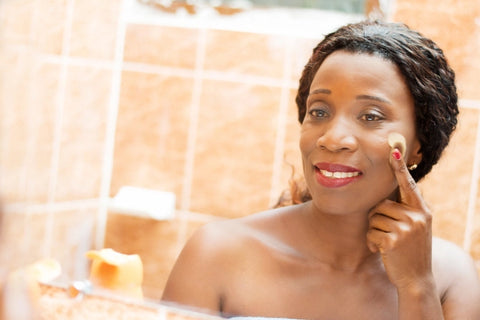 Black woman applying skincare product to her face to demonstrate how to exfoliate your face the right way