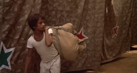 Boy in white shirt and pants carrying a sack in circus