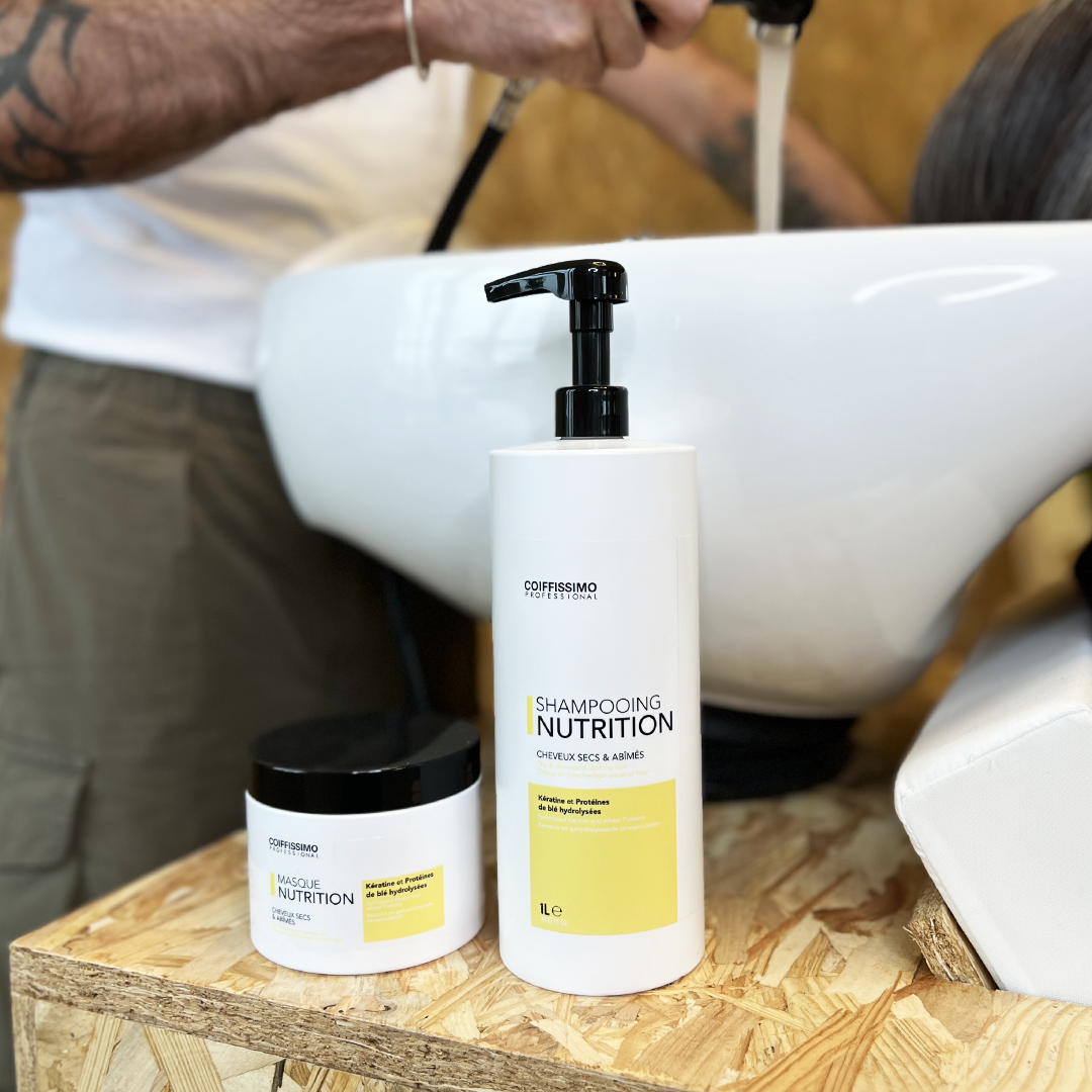 Shampoo and hair mask displayed near a salon sink with a stylist washing a client's hair.