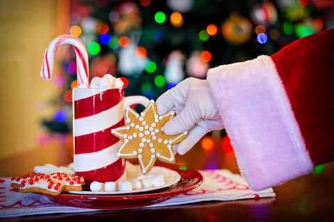 santa's hand grabbing a cookie with hot chocolate on a plate