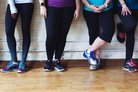 four women in yoga pants and tennis shoes leaning against a wall