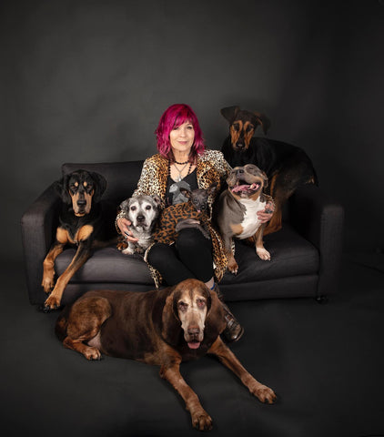 A woman with pink hair sitting with many dogs in a portrait setting